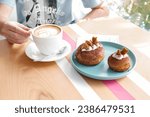 Man sitting holding a cup of coffee with two tiramisu doughnuts on plate at a cafe. 