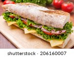 Long Ciabatta Sandwich with lettuce, slices of fresh tomatoes, ham, turkey breast and cheese cut in half