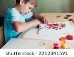 Small photo of 8 yeas old child sitting at desk and making picture from dry birch leaves. Boy using sponge to paint the leaves. Autumn activities for children