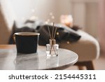 Bamboo sticks in bottle with scented candles and cup of tea on marble table closeup. Home aroma. Aromatherapy. Apartment living. 