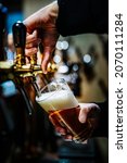 Small photo of bartender hand at beer tap pouring a draught beer in glass serving in a bar or pub