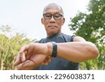 Small photo of Running Asian senior man checking his heartbeat with smartwatch at nature park. Mature Adult male checking pulse after jogging. Fitness tracker