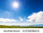 Small photo of sun shine on the blue sky. white fluffy clouds above the hilly mountain landscape. beautiful nature background on a sunny summer day at high noon