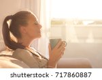 Pretty young woman sitting on sofa and enjoying first morning coffee on sunshine
