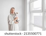 Happy Woman holds her beloved dog in her arms at home against white wall. Person with pet looking at camera