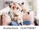 Happy woman playing with her dog on the couch at home. Dog licking middle aged woman in the living room