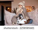Small photo of Frozen. Sad woman sit on couch at freezing cooled house in warm cap and blanket shiver tremble with cold. Unhappy middle aged lady spend time at home feel bad suffer of heating system problems