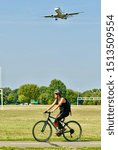 Small photo of Arlington, Virginia / USA - September 11, 2019: A woman rides her bicycle at Gravelly Point Park as a Jet Blue regional flight prepares to land at Ronald Reagan Washington National Airport.