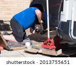 A kneeling mechanic has jacked up a motorhome recreational vehicle and removed a wheel and peers under the wheel arch checking the brakes.Trolley jack, socket set are visible