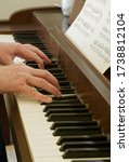 Small photo of TWINSBURG, OH, USA - MAY 13, 2020: Two hands on an old piano keyboard are playing a piece from sheet music.