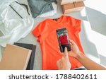 Selling online by taking photo of clothes with phone app and doing e-commerce business woman at home with shipping boxes.