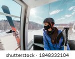 Ski resorts open for winter sports following coronavirus restriction guidelines. Woman tourist wearing face mask inside cabin lift on mountain slope going skiing.