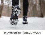 Winter exercise fitness lifestyle athlete walking with running shoes on snow and slippery ice needing traction soles on icy sidewalks. Run outside in cold weather.