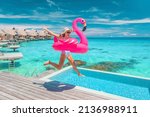 Luxury hotel beach vacation ocean overwater bungalows suite resort. Happy woman tourist jumping of joy in funny pool toy flamingo float excited to be in Bora Bora resort, French Polynesia.