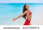 Small photo of Travel. Happy free summer vacation beach bikini body woman enjoying sun carefree with open arms sunbathing at Caribbean paradise beach wearing red bikini and beachwear skirt