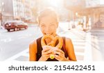 Small photo of Woman eating pretzel in Manhattan, a classic New York City snack. Multiracial asian young professional portrait smiling at camera