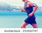 Cardio runner running listening smartphone music. Unrecognizable body jogging on ocean beach or waterfront working out with heart rate monitor app device and earphones in summer.