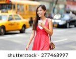 Urban woman drinking coffee happy smiling in New York City, Manhattan. Girl drinking hot drink from disposable cup walking in street wearing red dress. Biracial Asian Caucasian female model.