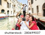 Travel couple taking selfie picture in gondola on Venice vacation. Beautiful lovers on a romantic boat ride across the Venetian canals taking self-portrait pictures with smartphone during holiday.