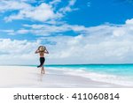 Luxury travel woman in black beachwear sarong walking taking a stroll on perfect white sand Caribbean beach. Girl tourist on summer holiday holding sun hat at vacation resort. Tropical landscape.