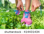 Healthy active lifestyle woman athlete tying running shoes. Happy sporty runner girl lacing shoelaces on pink fashion sneakers on summer grass in city park getting ready for a fitness morning jog.