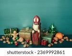 Chocolate figurine of St. Nicholas with gifts against a blue wall. Holiday background Saint Nicholas, Sinterklaas, gifts for children with cookies, chocolate, nut, tangerines and sweets