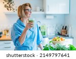 Small photo of Smiling middle aged woman with just made glass of detox shake, green smoothie in the kitchen. Healthy dieting, eating, cooking. Natural anti aging methods, weight loss program. Vegan, vegetarian diet