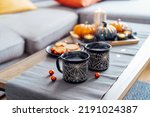 Cozy halloween plans at home. Hot tea drink in black mugs with spider net pattern, cookies and and sweets on the plate, pumpkin decor on the coffee table. Festive autumn, fall mood home decor