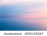 Idyllic seascape with pink evening color. The calm sea reflects the clear sky like a mirror. Blue pink sea background