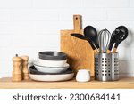 Kitchen table, kitchen utensils, plates, bowls, shakers and wooden cutting board.