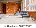 Small photo of Arranged new grey plumbing sewer pipes are laid down on the floor waiting to be installed, view on scaffolding through the window of building under construction.