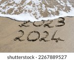 New Year 2024 is coming concept - inscription 2023 and 2024 on a beach sand, the wave is starting to cover the digits 2023